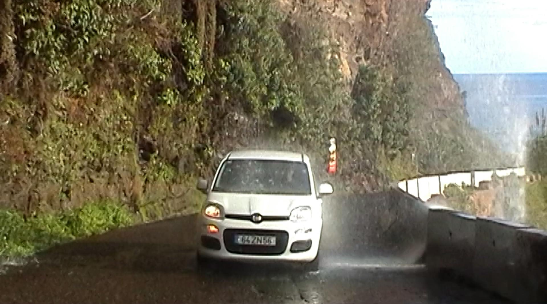 a white car driving down a road next to a cliff