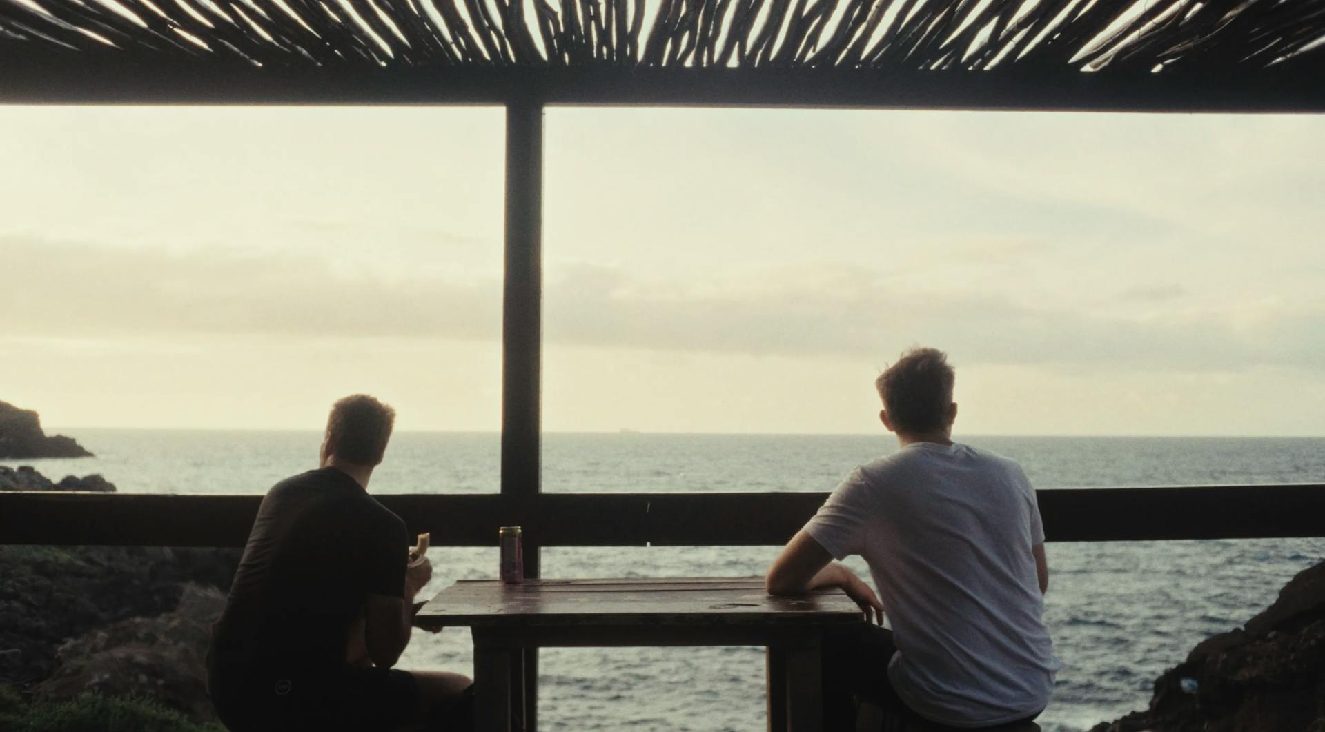 two men sitting at a table looking out at the ocean