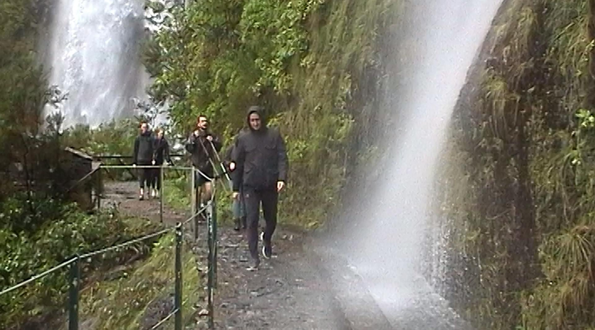 a group of people walking down a path next to a waterfall