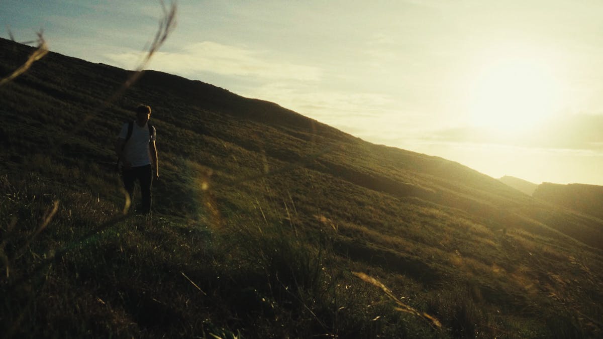 a person walking up a hill with the sun behind them